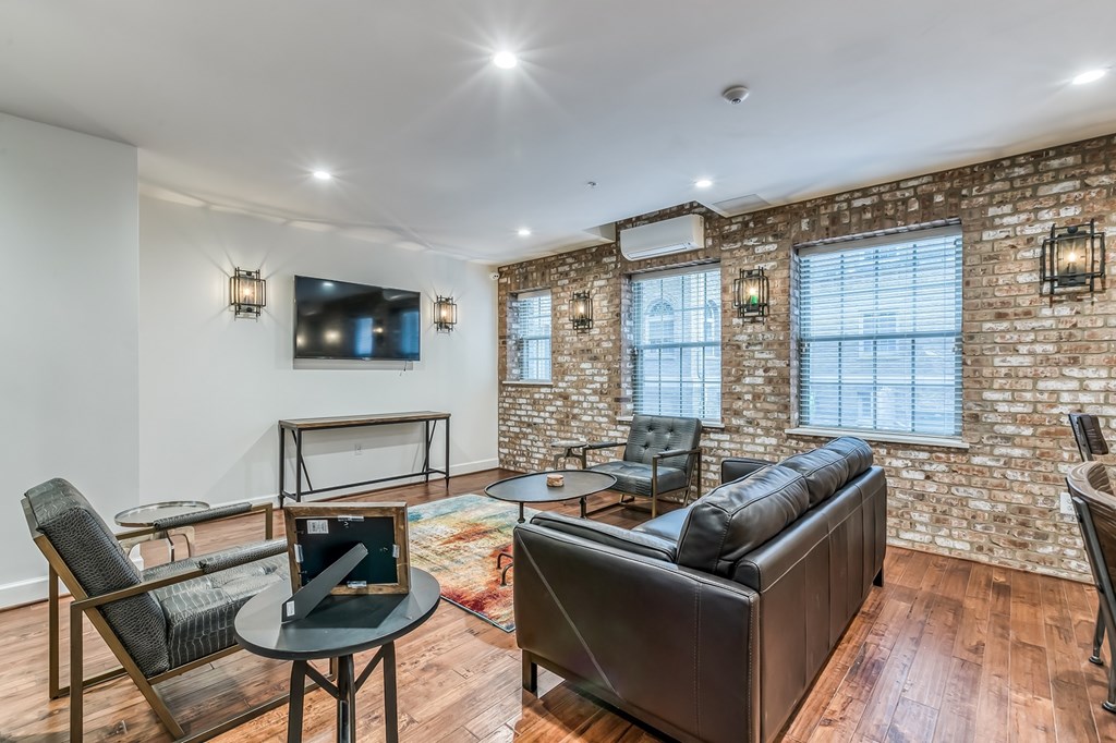 A living room with a brick wall and a black leather couch.