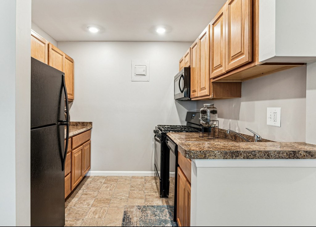 A kitchen with a black refrigerator and a granite countertop.
