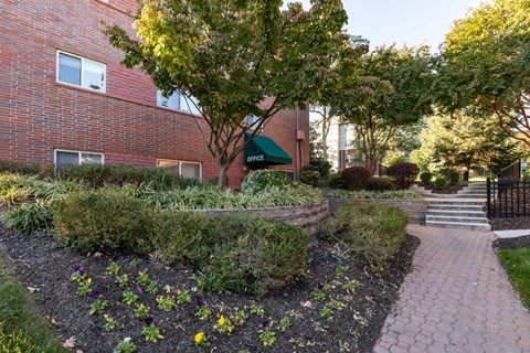 a walkway in front of a brick building with trees and plants