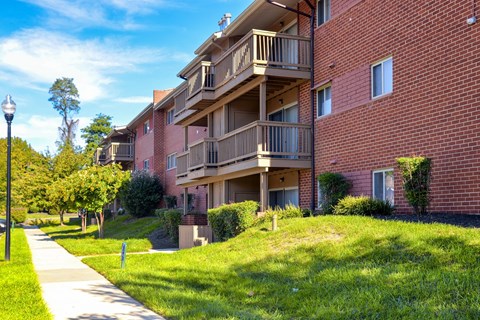 A red brick apartment building with balconies and a sidewalk in front.