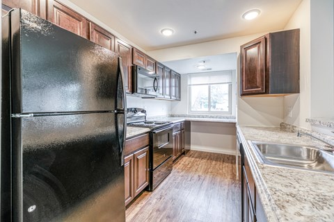 A black refrigerator is in a kitchen with wooden cabinets.