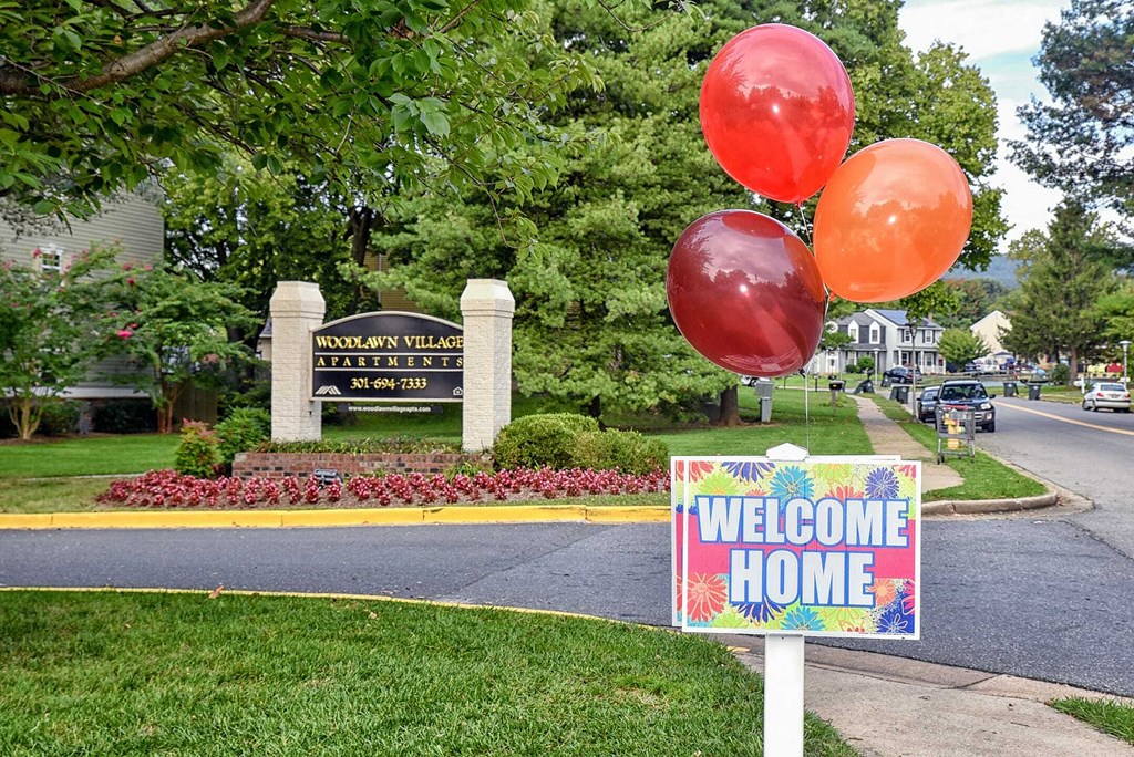a sign that says welcome home in front of a lawn with balloons