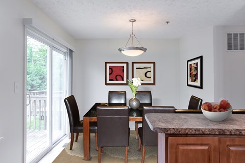 A dining room with a table set for two and a bowl of fruit on the counter.