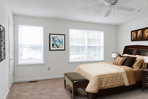 A bedroom with a bed, a bench, and two windows.