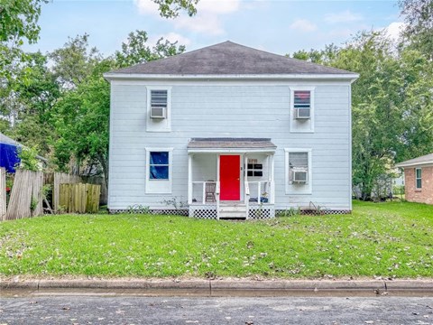 A white house with a red door is surrounded by greenery.