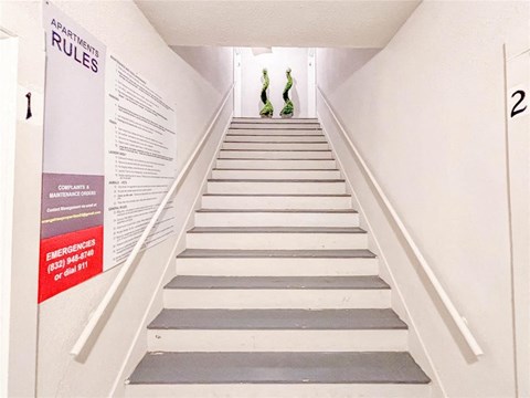 A staircase with a sign on the wall that says "APARTMENT RULES".