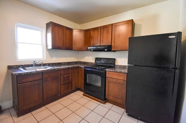 A black refrigerator stands in a kitchen with wooden cabinets and a black oven.