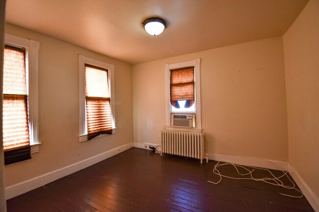 A room with a window, a radiator, and a white cord on the floor.