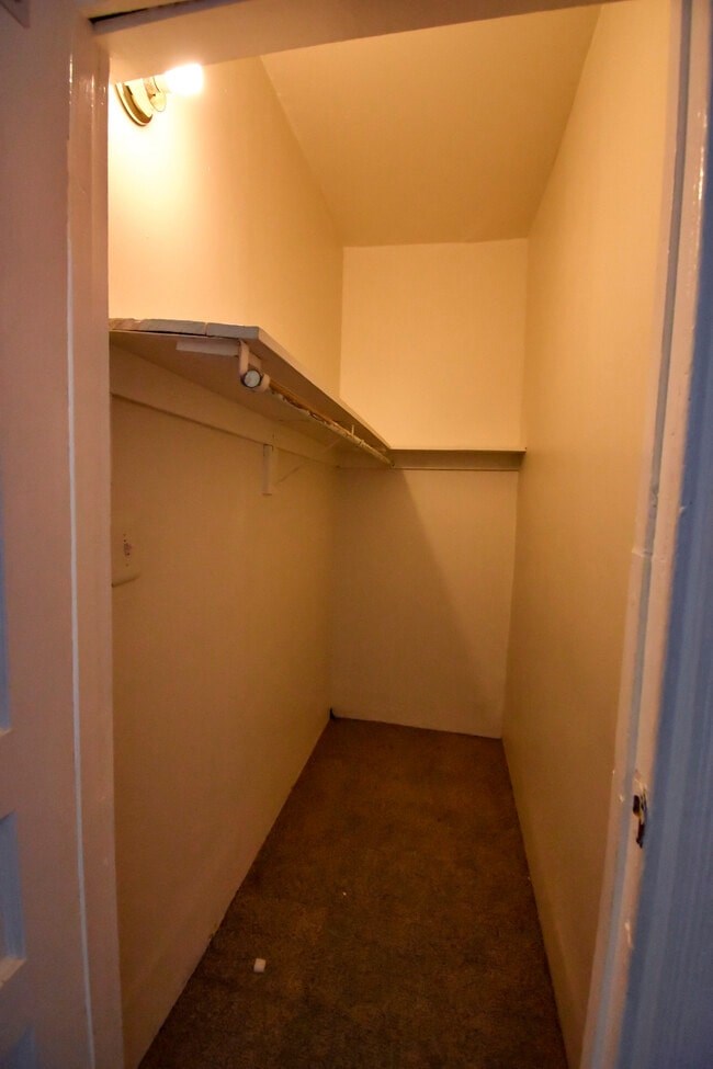 A small, empty room with a white door on the left and a white shelf on the right.