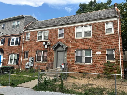 A red brick house with a grey roof and a grey fence in front.