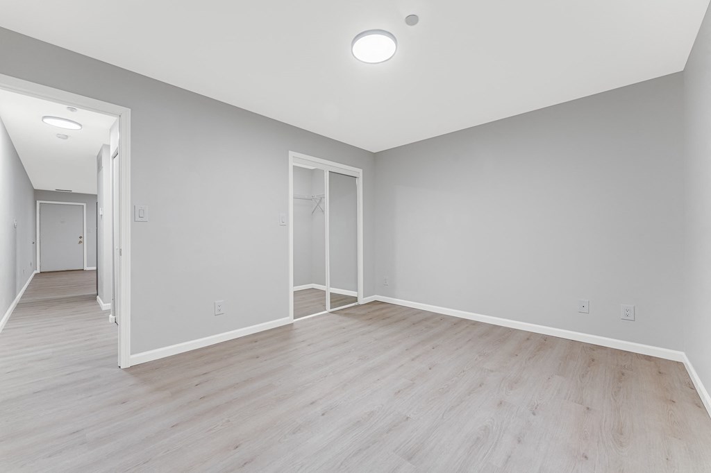 A spacious room with a white ceiling and light wood flooring.