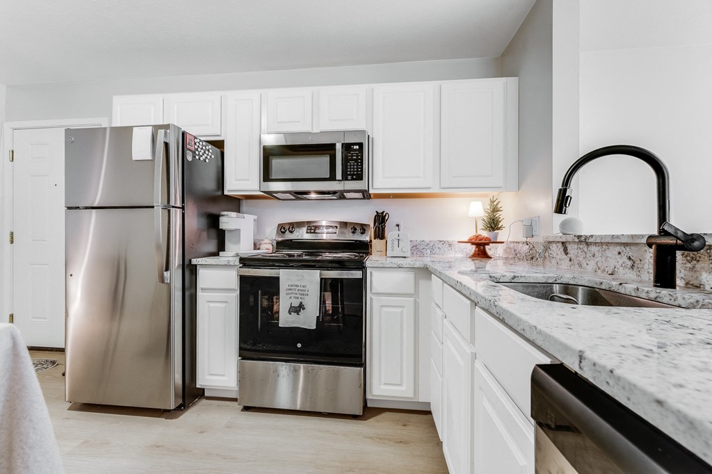 A kitchen with a refrigerator, microwave, oven, and sink.