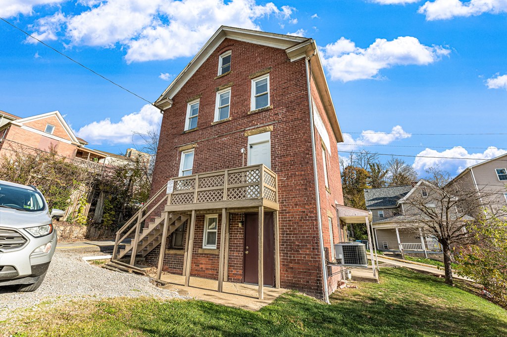 A red brick house with a porch and a car parked in front.