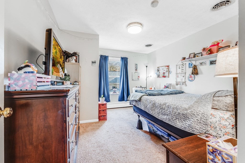 A bedroom with a bed, dresser, and window with blue curtains.