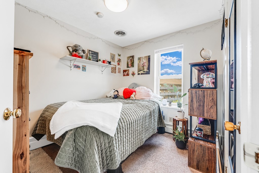 A bedroom with a bed, a window, and a shelf with various items.