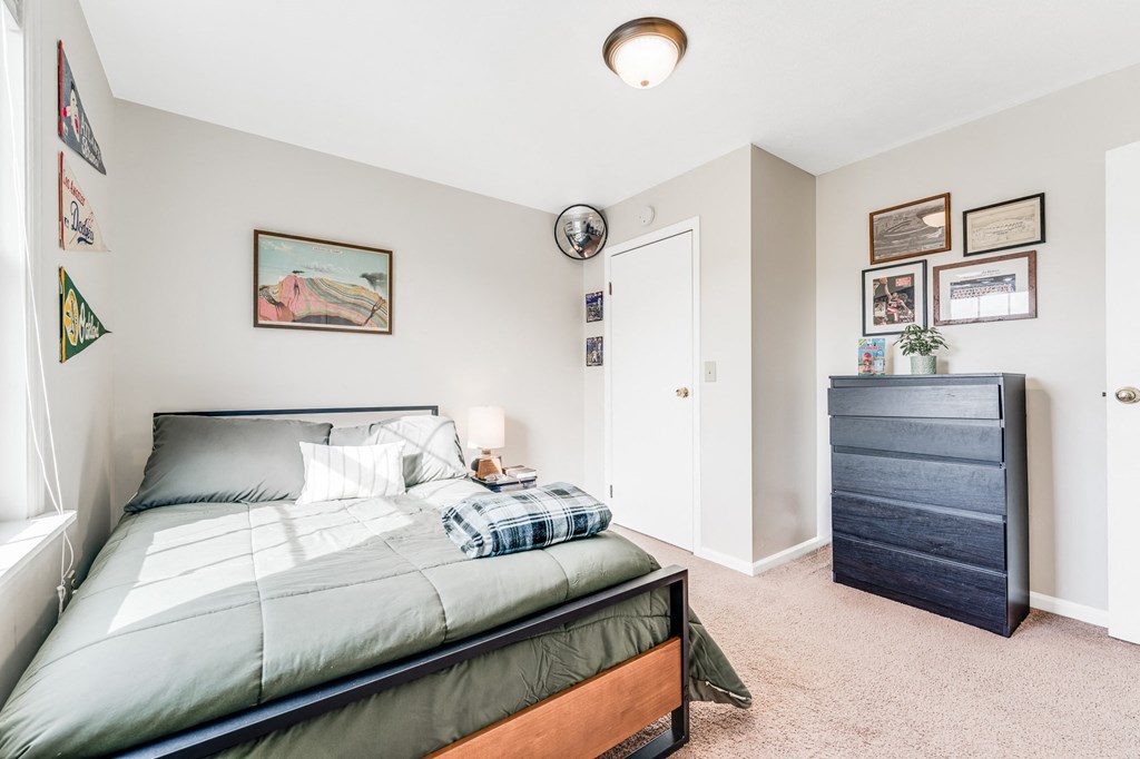 A bedroom with a bed, dresser, and a painting on the wall.