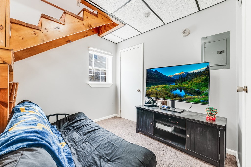 A sofa with a blue blanket in a room with a television and a wooden staircase.