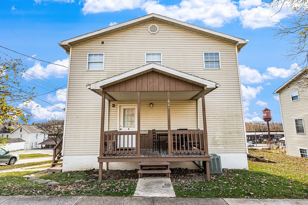 A beige house with a brown porch and a green lawn.