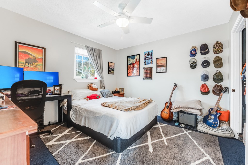 A bedroom with a bed, guitars, and a ceiling fan.