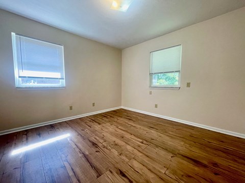 an empty living room with wooden floors and two windows