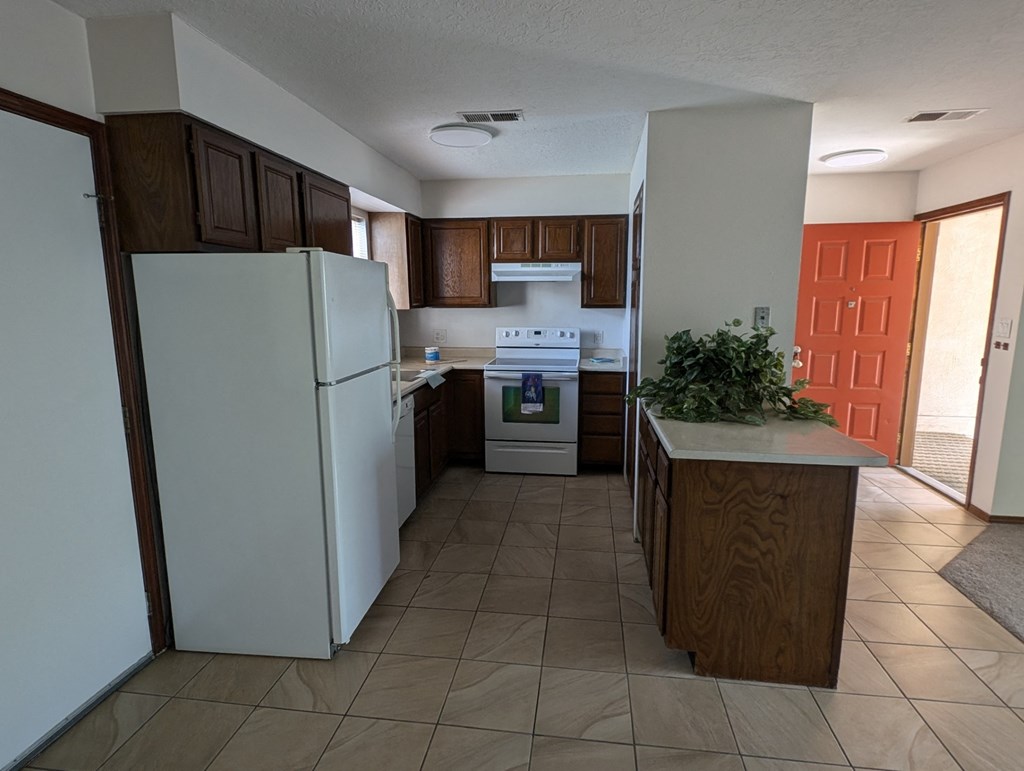 an empty kitchen with white appliances and brown cabinets