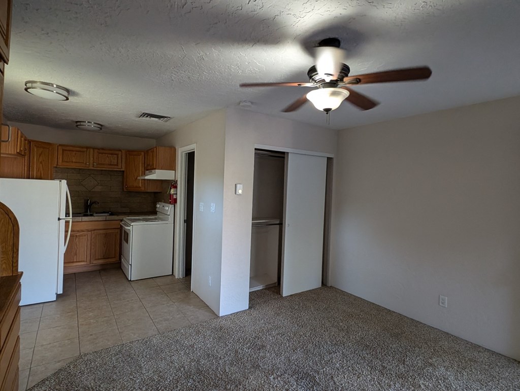 an empty living room with a ceiling fan and a kitchen