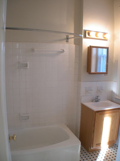 A white tiled bathroom with a white tub and sink.