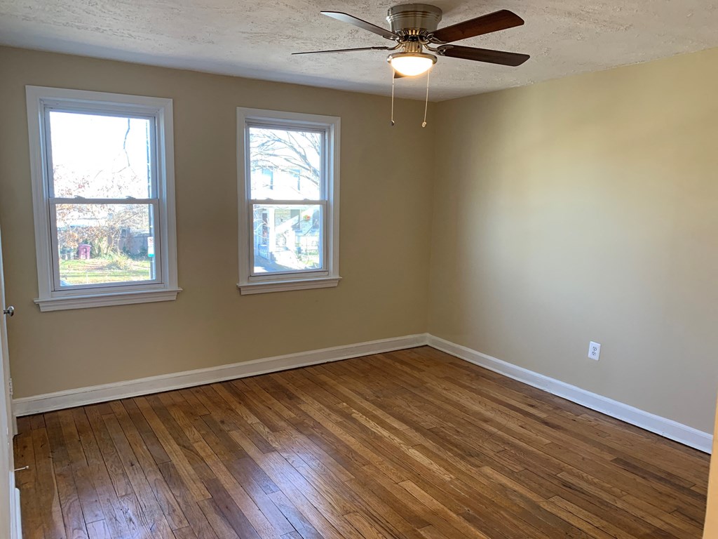 A room with a ceiling fan and two windows.