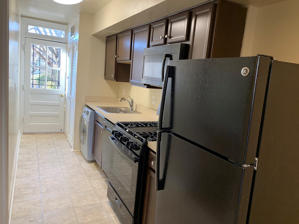 A black refrigerator stands in a kitchen with a stove and washing machine.