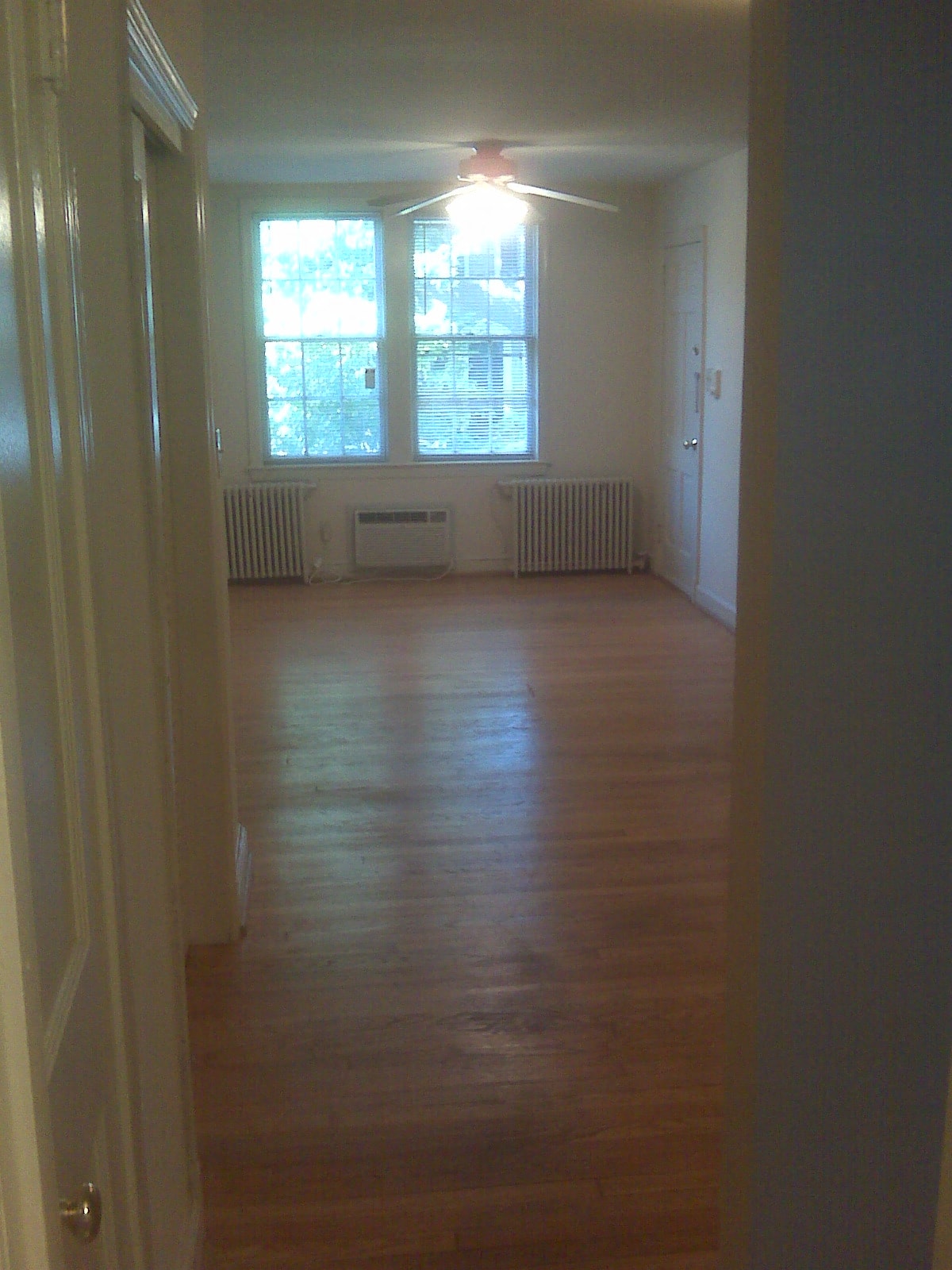 A long hallway with a door on the left and a window with two radiators on the right.