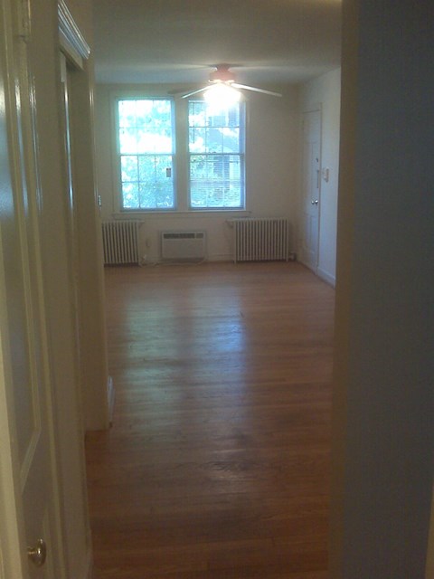 A long hallway with a door on the left and a window with two radiators on the right.
