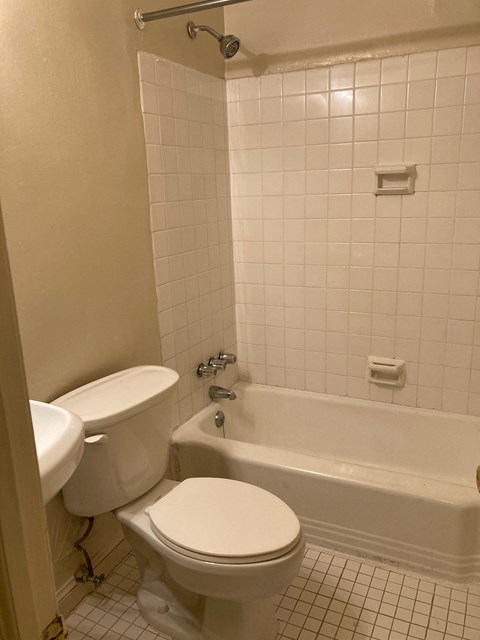 A white toilet and bathtub in a bathroom with white tiles.