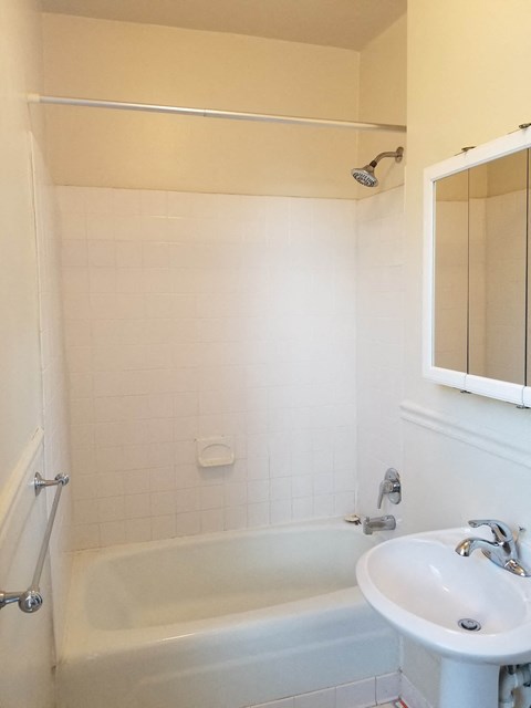 A white bathroom with a tub, sink and mirror.