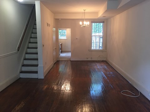 A room with wooden floors and a staircase on the left side.