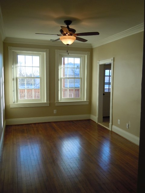 A room with a ceiling fan and two windows.