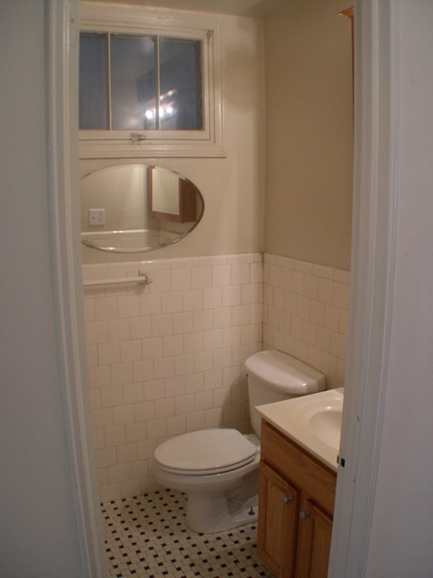 A white toilet sits in a bathroom with a sink and mirror.