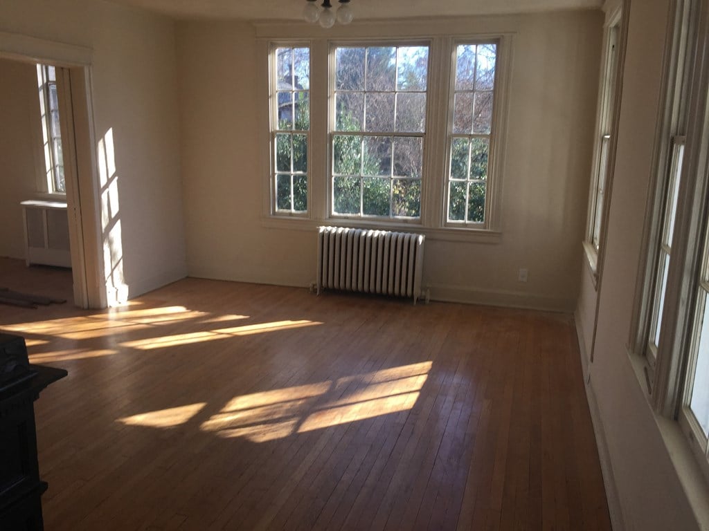 A room with wooden floors and a large window with sunlight coming through.