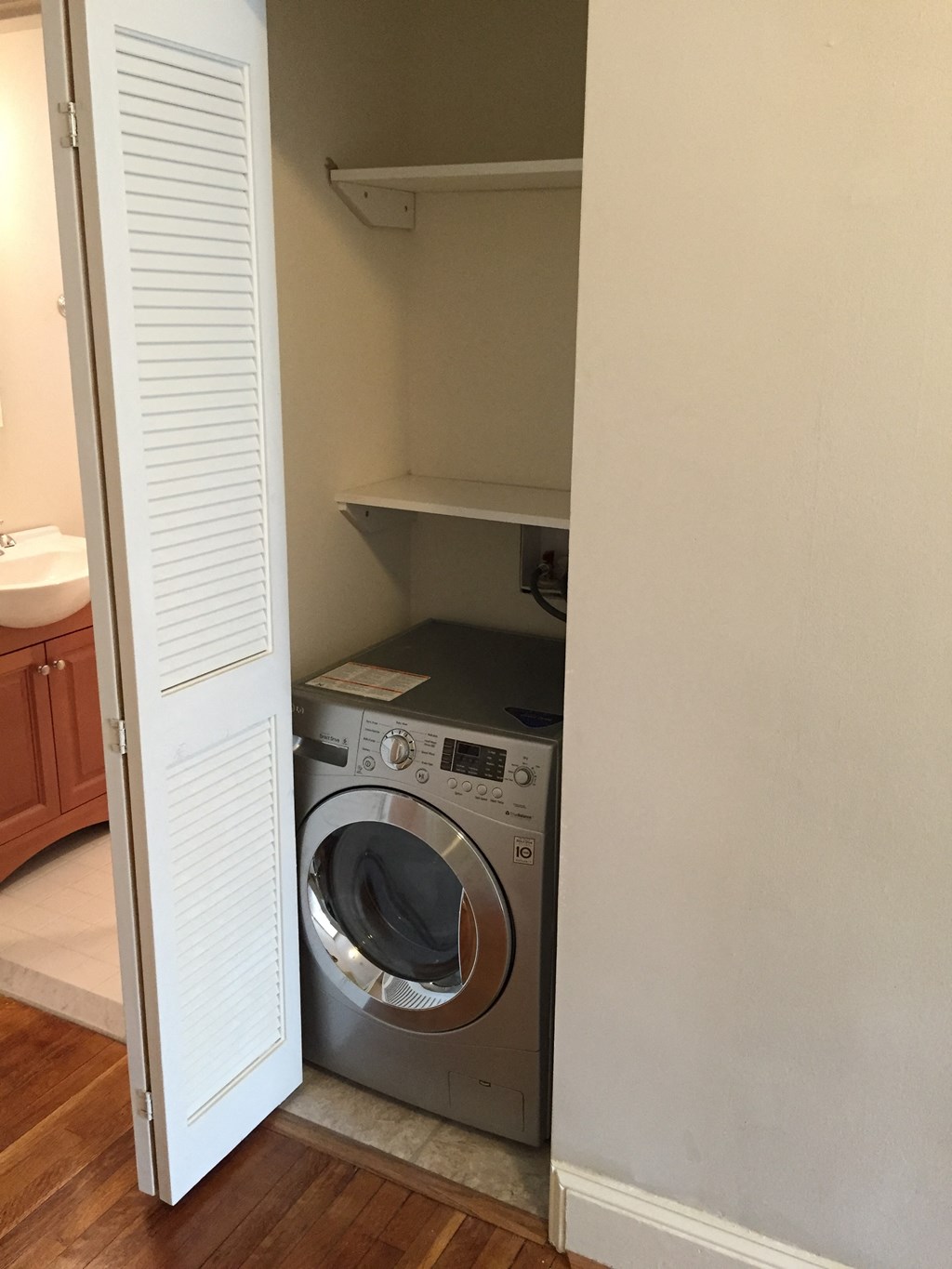 A washing machine is in a small space between a wall and a cabinet.