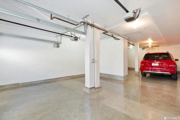 A red car is parked in a garage with a white pillar in the middle.