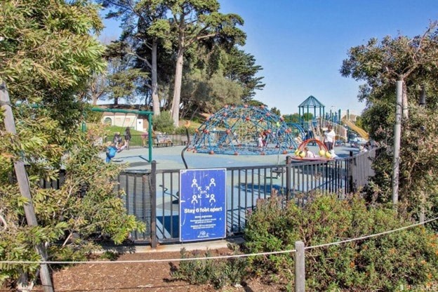 A sign with a blue background and white text is in front of a playground.