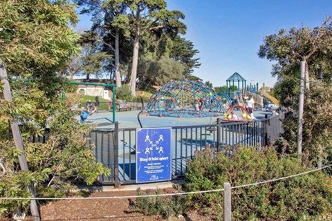 A sign with a blue background and white text is in front of a playground.