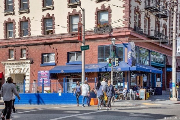 A street view with people walking and a blue awninged building.