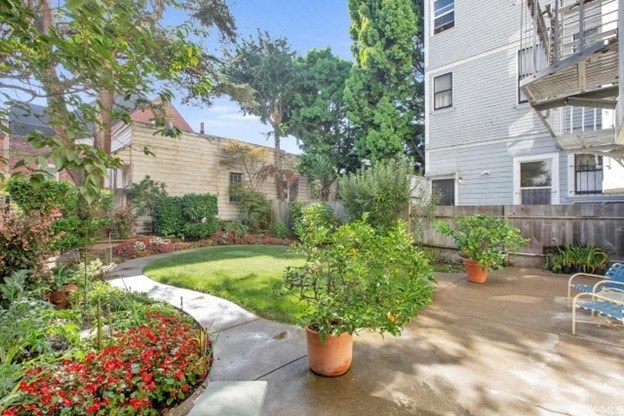 A sunny day in a garden with a bench and a building in the background.