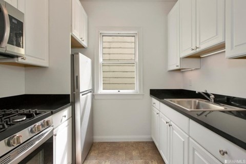A kitchen with white cabinets and black countertops.