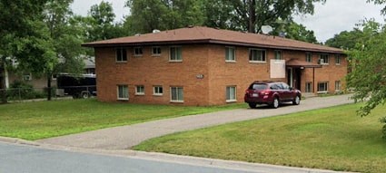A red car is parked in front of a brick house.