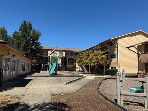 A playground area with a green slide in front of a building.