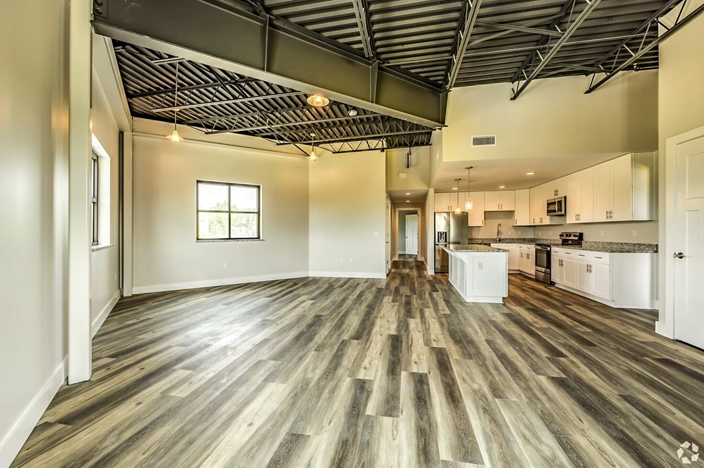 A spacious room with wooden flooring and a kitchen area in the background.