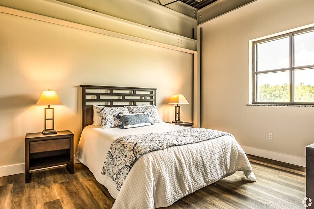 A bedroom with a bed, two lamps, and a window.