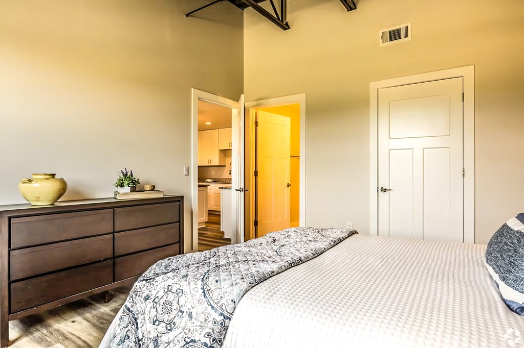 A bedroom with a bed, dresser, and two doors.