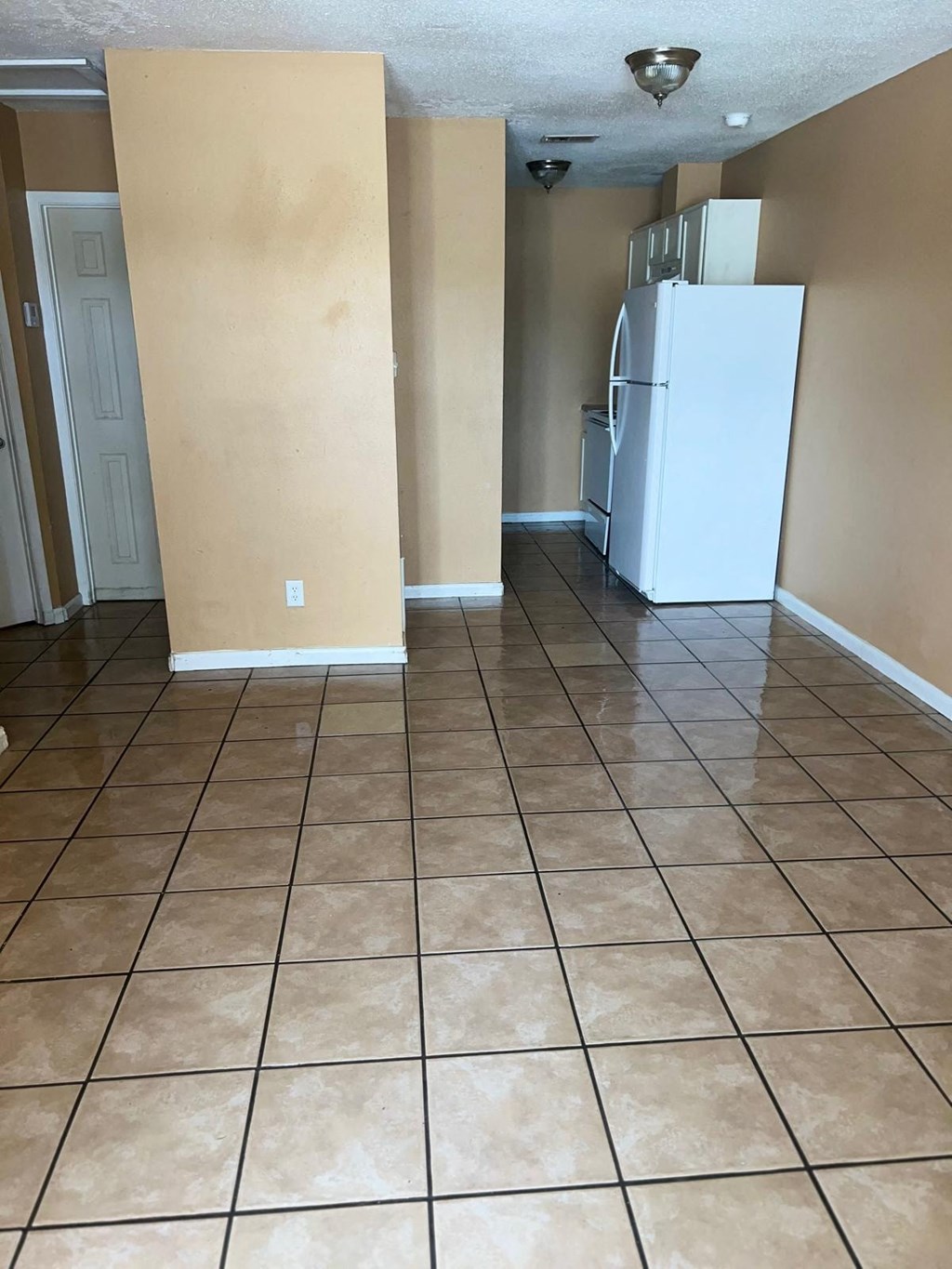 an empty kitchen with a refrigerator and a tiled floor